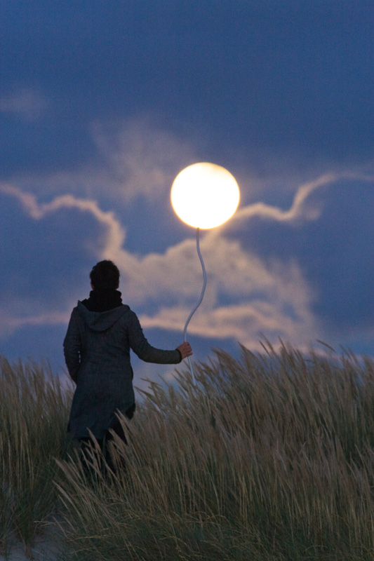 Un personnage tient la Pleine Lune au bout d'un fil, comme un ballon de baudruche.